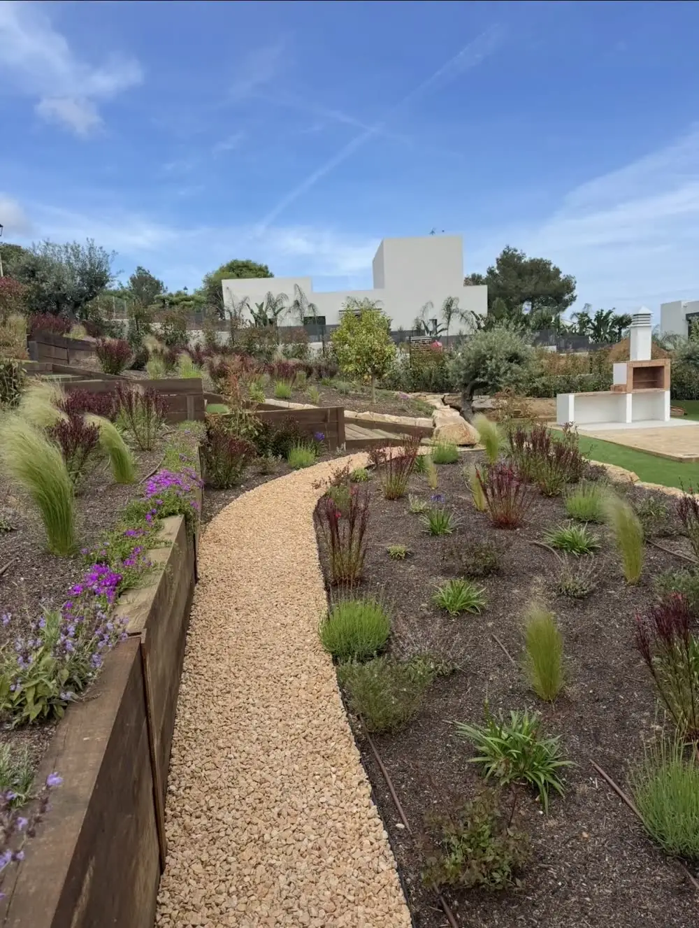 Jardín mediterráneo de Vida Verde con senderos, bancales y una vivienda blanca